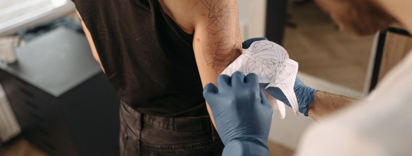 Tatuatore applica lo stencil sul braccio di una cliente